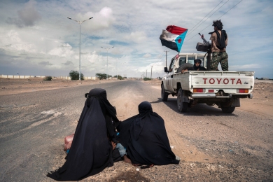 Aden, Yemen. December 2020. Southern Transition Council (STC) soldiers drive at speed past two begging Muhamasheen women in Lahj, Yemen. The Muhamasheen caste have long been considered the most marginalized people in Yemen and treated as social outcasts. Despite numbering over 3 million in the country today, the Muhamasheen are often denied healthcare, education and even identification cards.  Giles Clarke for UN/OCHA